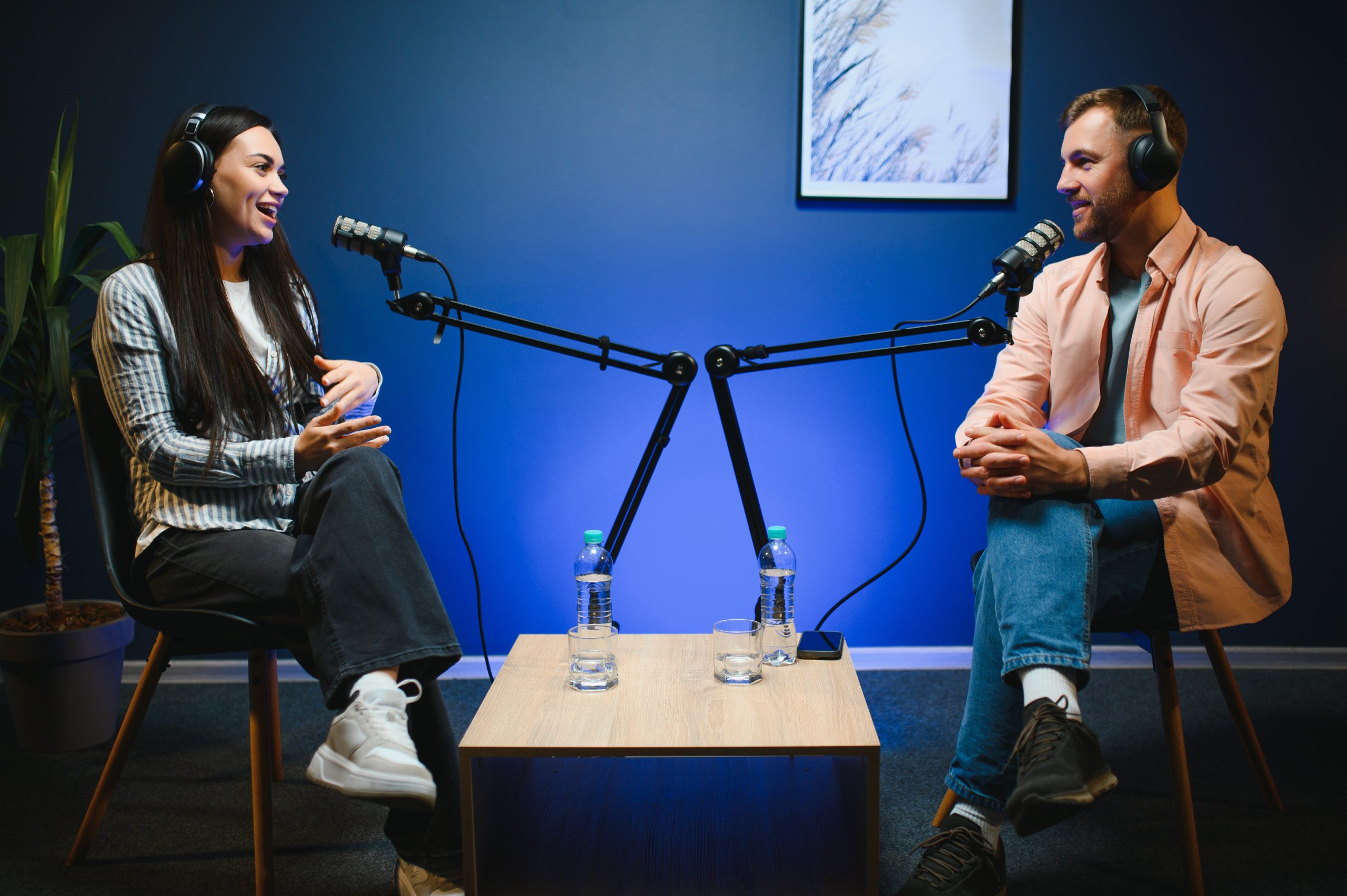 Female podcaster in headphones interviewing man guest using microphone, smiling, recording and broadcasting audio podcast in studio. Content creator, blogging.
