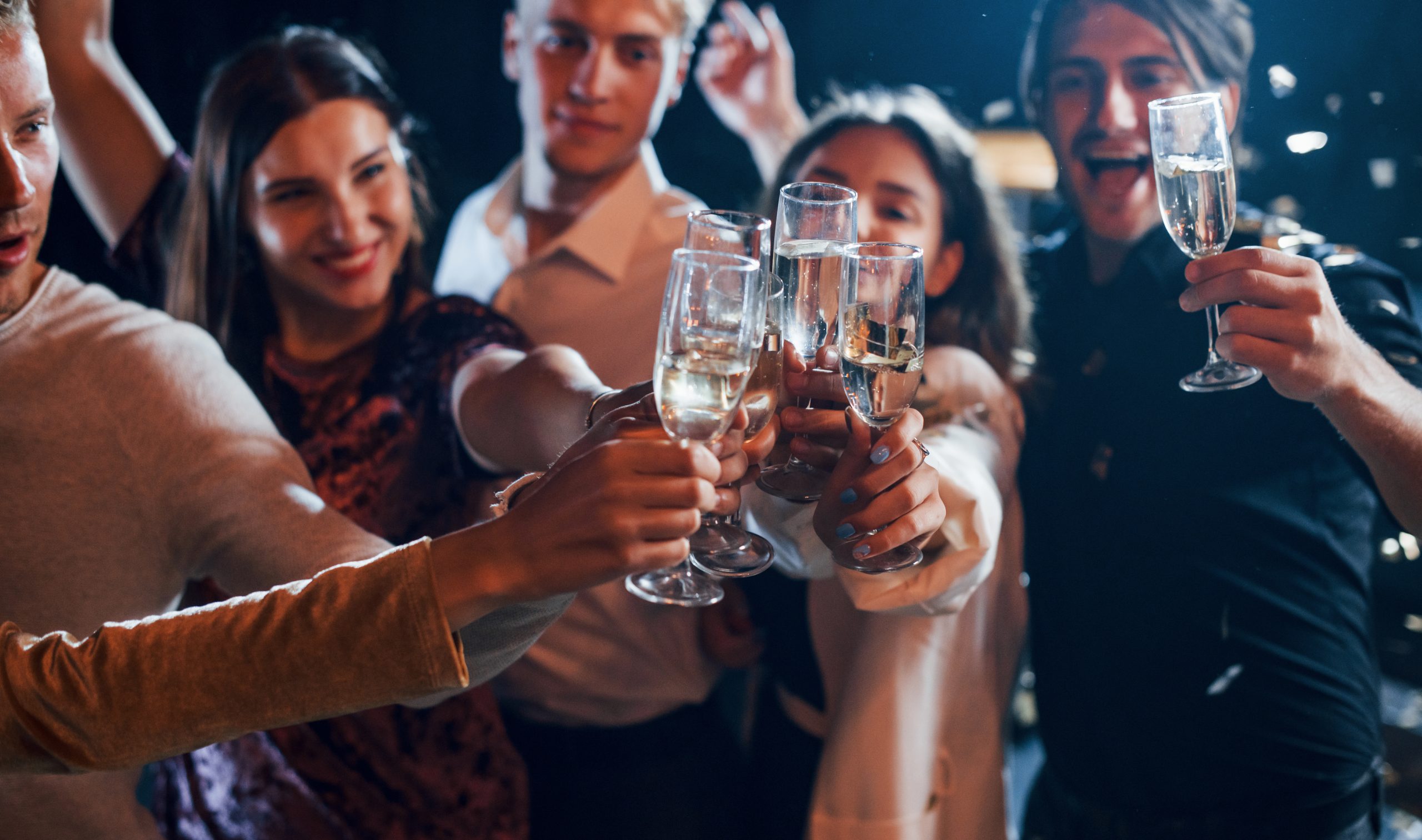 Group of cheerful friends celebrating new year indoors with drinks in hands.